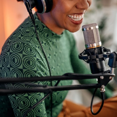 Selective focus of mouth of young smiling women recording podcast and doing live streaming using microphone and headphones in recording studio