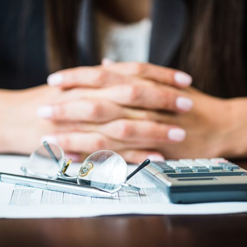 Close up of businesswomans hands with pen, glasses, and calculator doing some financial calculations